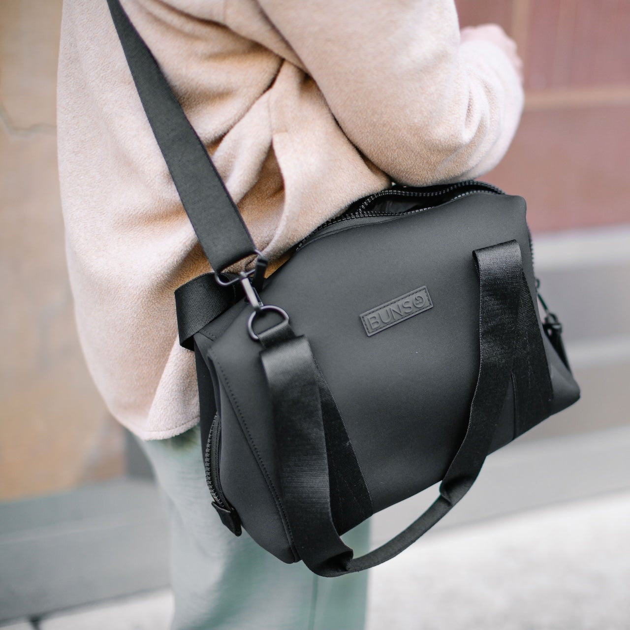 A person wearing a black duffel diaper bag on their shoulder.