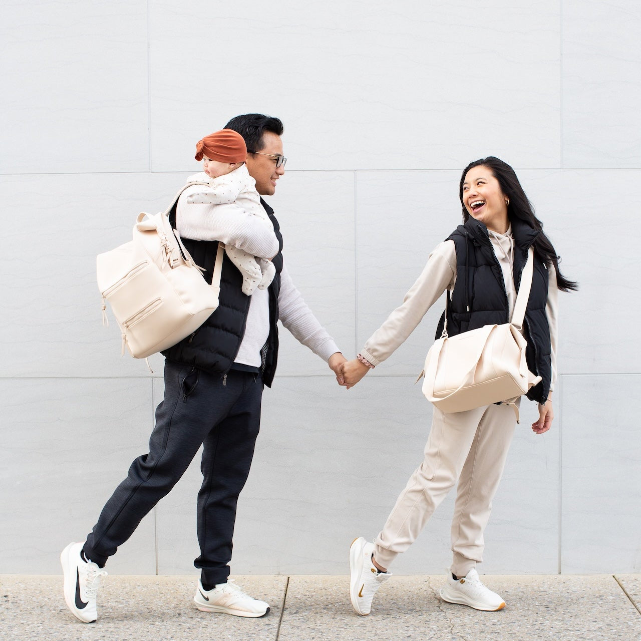 A family walking together, holding hands, wearing cream diaper bags