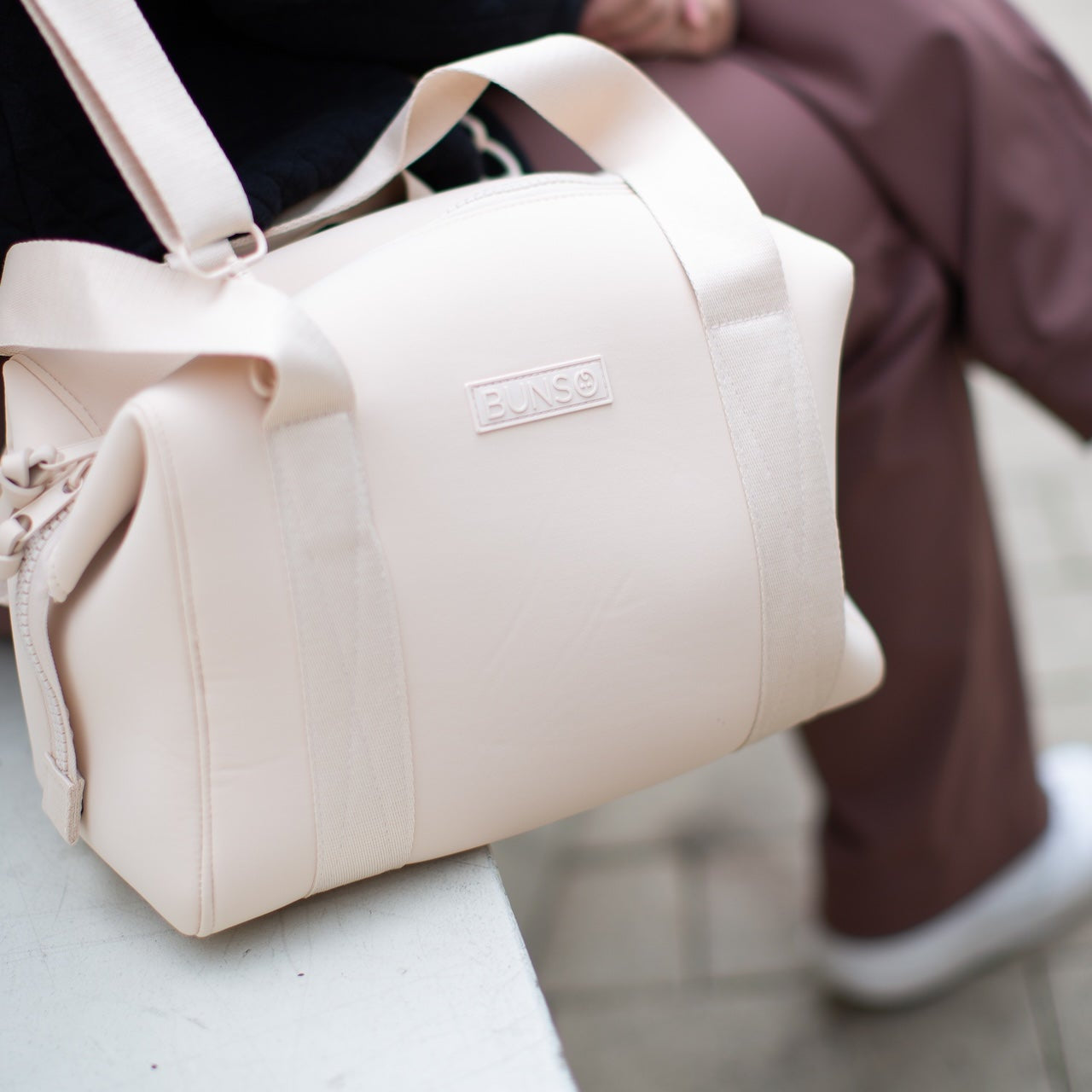 A person wearing a cream duffel diaper bag while sitting