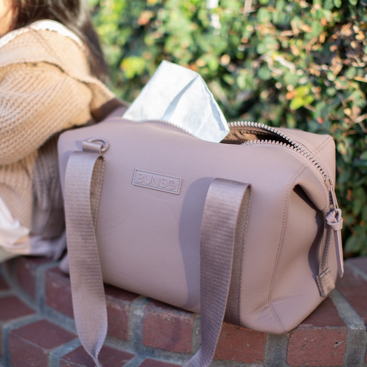 A mauve duffel bag beside a child sitting on a brick ledge
