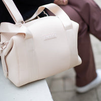 A person wearing a cream duffel diaper bag while sitting