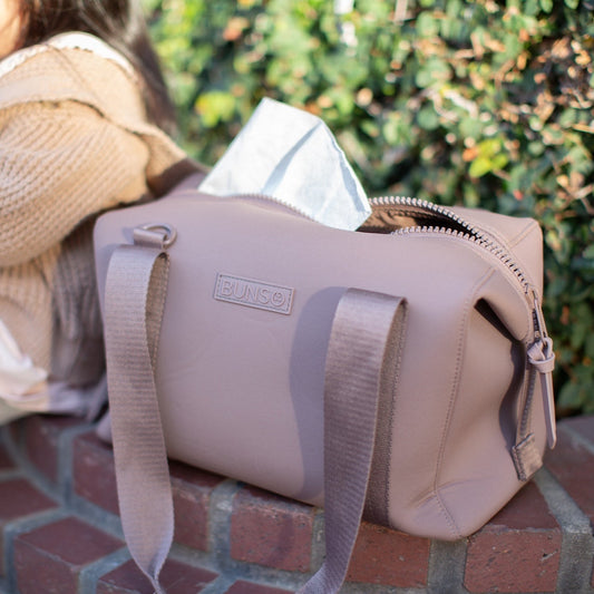 A mauve duffel bag beside a child sitting on a brick ledge
