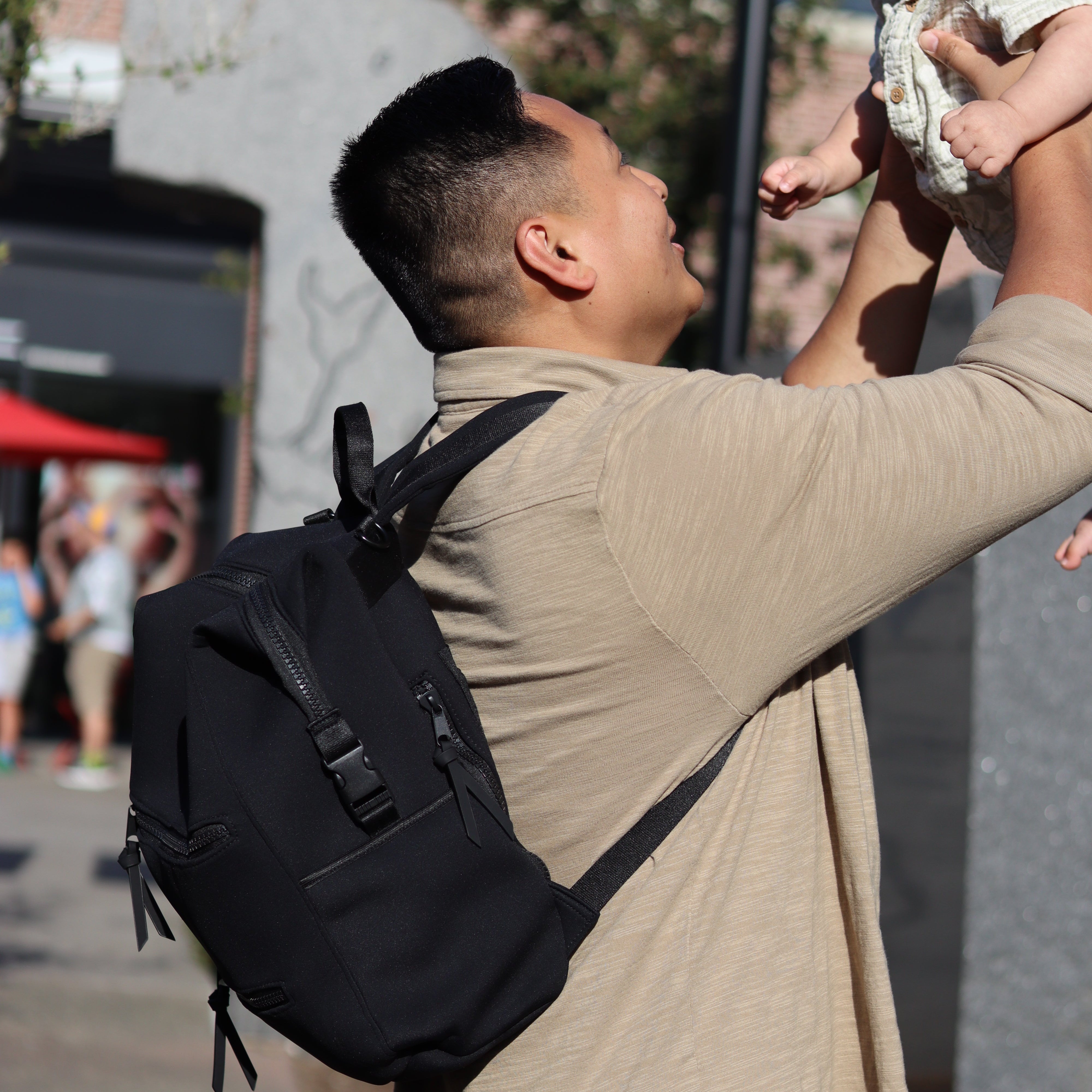 Man holding a baby with a black bag over his shoulder outdoors