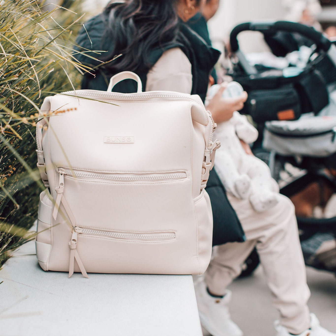 Woman with a beige backpack and child in front of strollers outdoors